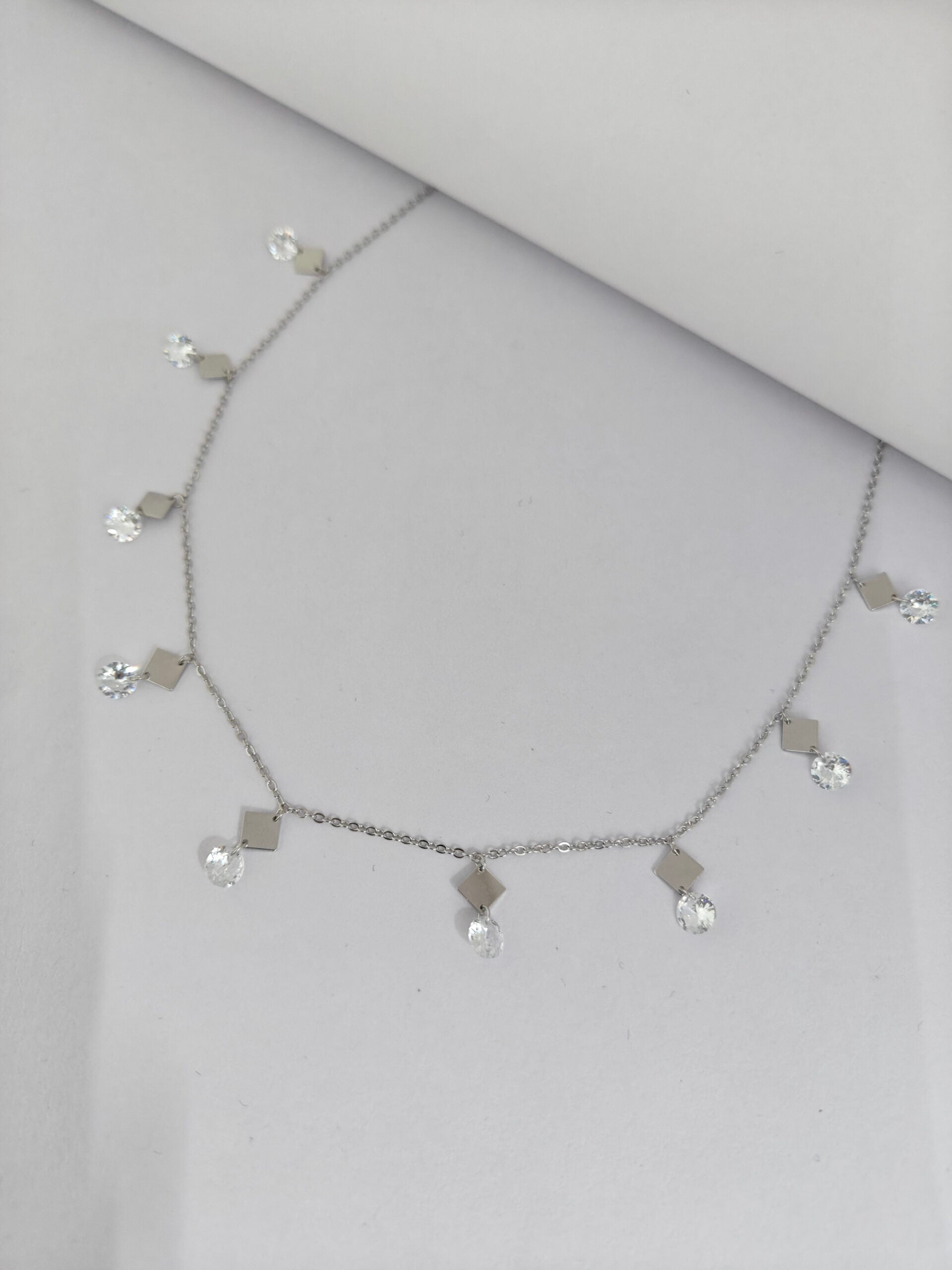 Silver necklace with small pendants on a light gray background